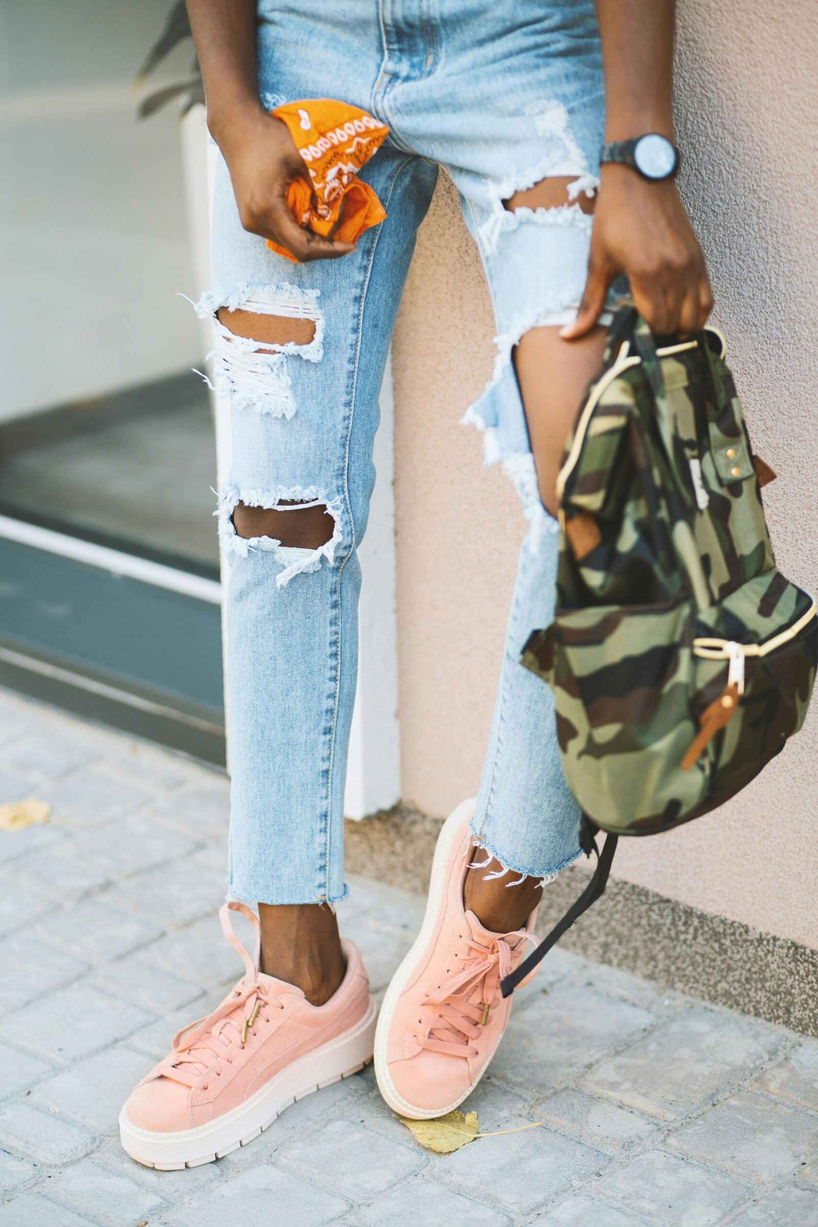 Fashionable young woman in ripped jeans and pink sneakers outdoors.