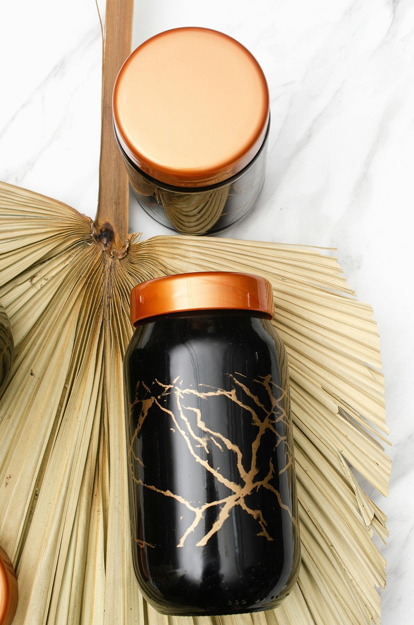 Elegant black jars with copper lids displayed on a natural palm leaf setting, perfect for modern decor.